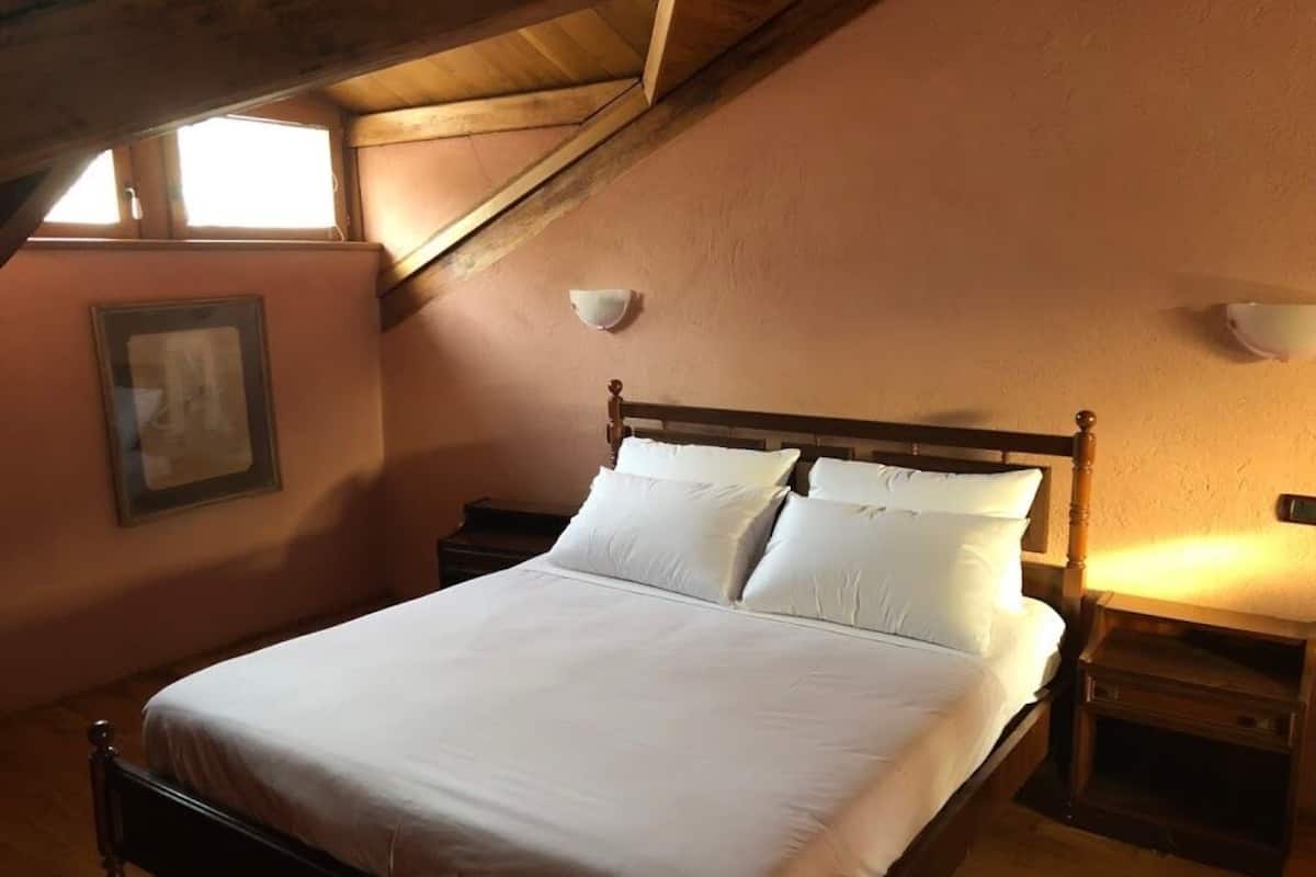A bedroom with a wooden bed, white bedding, a nightstand, and a wall-mounted light fixture.