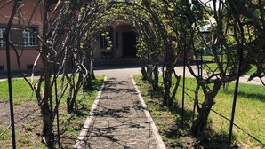 Un sentiero conduce a un edificio con un portico coperto, immerso tra alberi e prati.