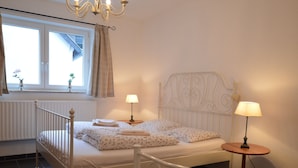 A bedroom with a white metal bed frame, two bedside tables with lamps, a window with curtains, and a radiator. - A Modern Holiday Home for 2-5 People River Mosel (Moselkern)