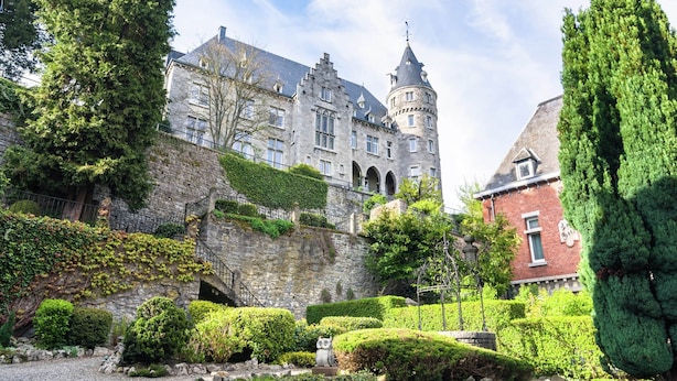 Un bâtiment historique doté d’une tourelle, de murs en pierre et d’un jardin bien entretenu, agrémenté de haies et d’arbres.