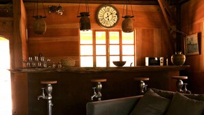 A rustic wooden interior with a wooden-framed window, a clock, and a bar area with stools. -  Mimosa chalet Indonésie. (Essaouira)