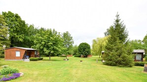 A grassy area with a small wooden cabin, a large tree, and a small shed.