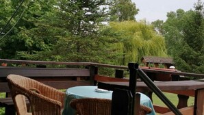 A wooden deck with wicker chairs and a table, surrounded by lush greenery and trees.