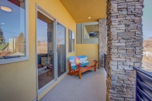 A balcony with a stone wall, a wooden bench, and a glass door leading to a room. - Downtown Skyline Rooftop Patio Modern Townhome (Colorado Springs)