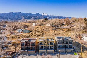 A multi-story residential building with a central staircase, surrounded by a hilly landscape with sparse vegetation and distant mountains. - Downtown Skyline Rooftop Patio Modern Townhome (Colorado Springs)