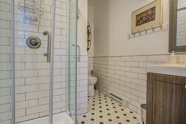 Un baño con cabina de ducha de vidrio, paredes con azulejos blancos, un inodoro y un armario de madera.