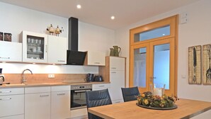 A modern kitchen with white cabinets, a built-in oven, and a dining area with a wooden table and black chairs.