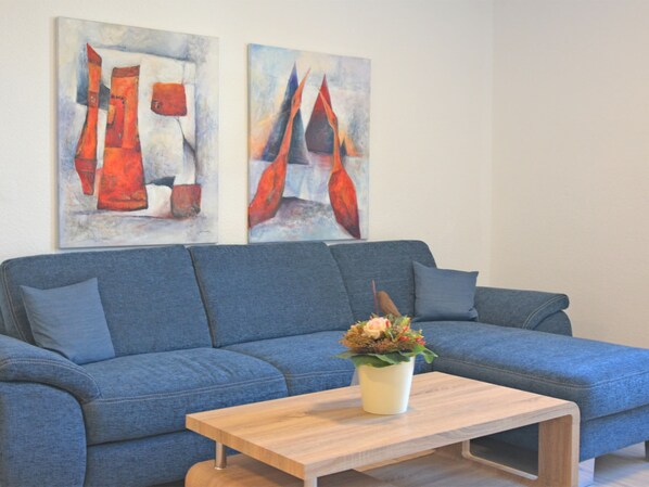 Um sofá azul com uma mesa de centro de madeira e duas pinturas abstratas na parede.