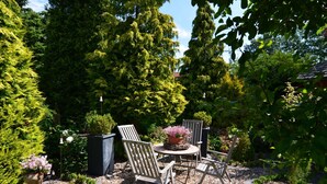 A garden patio with a table and chairs, surrounded by trees and shrubs.