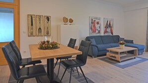 A modern living room with a dining table, blue sofa, and artwork on the walls.