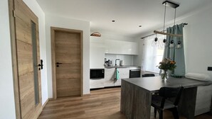 A modern kitchen with white cabinets, a wooden door, and a dining area with a table and chairs. - Ferienhaus mit Sauna in Skigebietsnahe (Drachselsried)