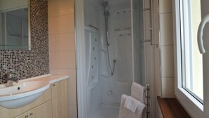 Een moderne badkamer met een douche met glazen wand, een beige wastafel en een houten opbergmeubel.