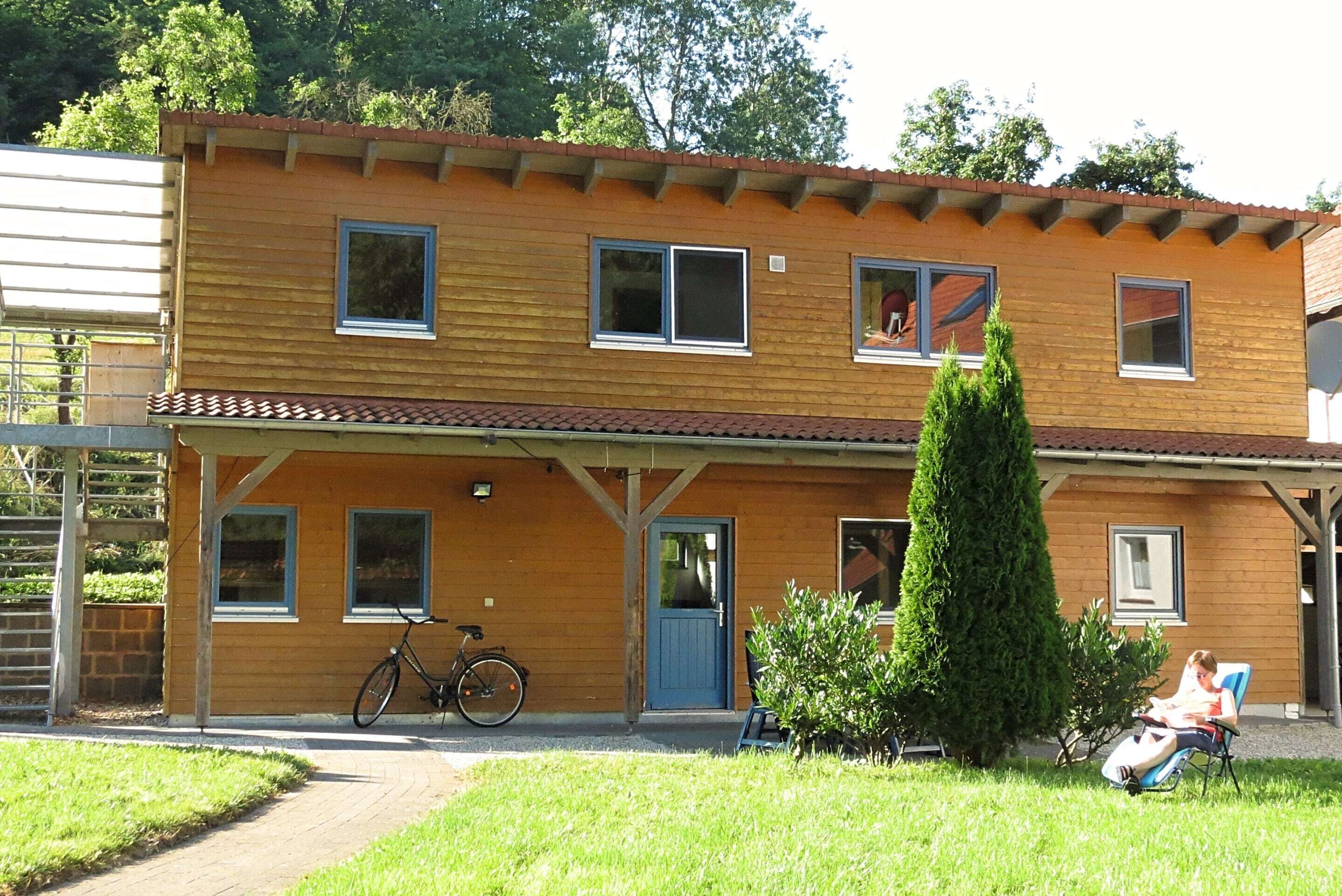 A two-story wooden building with a balcony, a bicycle, and a person sitting on a chair.