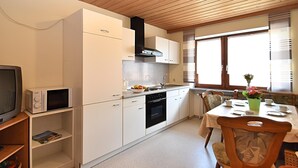 A compact kitchen with white cabinets, a microwave, a stove, and a dining area with a table and chairs. - Apartment in Bavaria Near Forest (Gleissenberg)