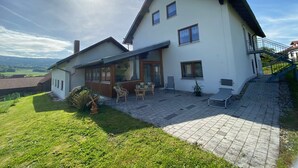 A two-story house with a patio area, a small garden, and a view of the countryside. - Apartment in Bavaria Near Forest (Gleissenberg)