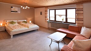A bedroom with a bed, a nightstand, a dresser, a window with blinds, a radiator, and a sofa. - Apartment in Bavaria Near Forest (Gleissenberg)