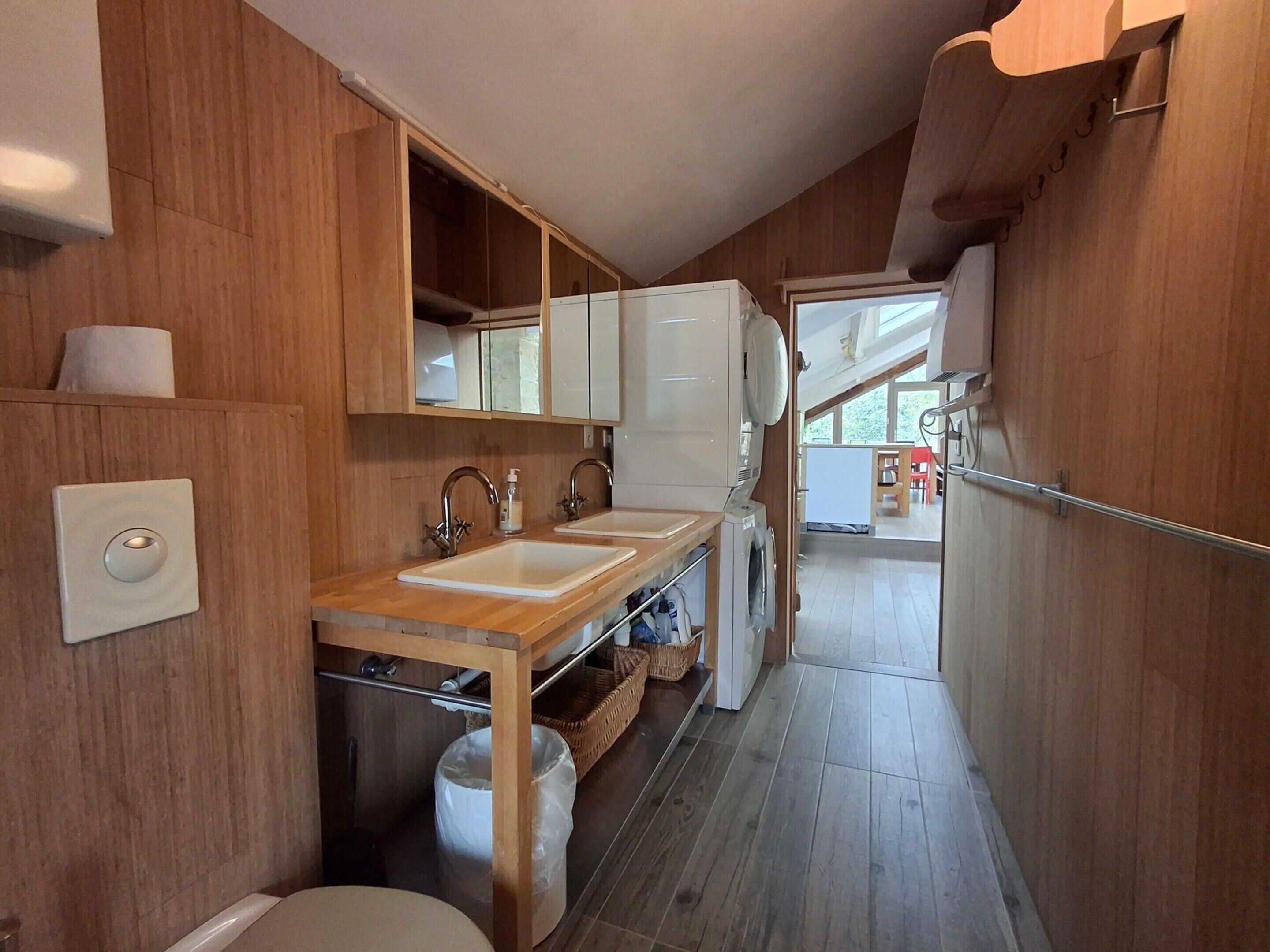 Eine kleine Küche mit Holzwänden, einem Spülbecken, einer Waschmaschine und einem kleinen Fenster.