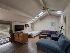 A spacious living room with a large blue sofa, a wooden coffee table, and a television on a wooden cabinet. There is a skylight above the sofa and a ceiling fan. - Fairytale Escape in Lamorteau (Rouvroy)