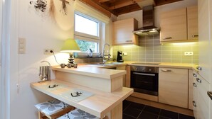 A modern kitchen with wooden beams, a built-in oven, and a window providing natural light. - Cottage in Durbuy With Terrace, Garden (Durbuy)