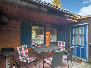 Um alpendre de madeira com mesa, cadeiras, churrasqueira e uma porta azul.