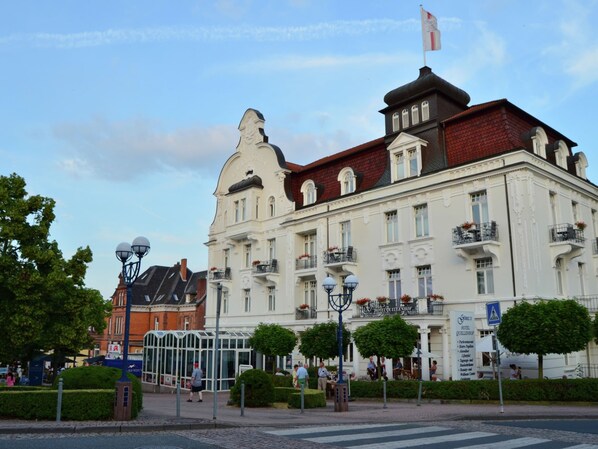 A historic building with a prominent clock tower, multiple balconies with flower boxes, and a sign indicating it is a hotel.