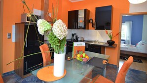 Une cuisine moderne aux murs orange, un coin repas avec une table en verre et un lit dans la pièce adjacente.