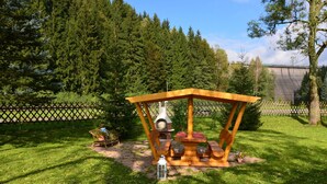 A wooden outdoor seating area with a table and benches, surrounded by a fence and trees. - Apartment Nahe Erzgebirge fur 2 Personen (Neuhausen)