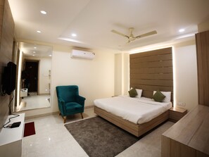 A modern bedroom with a bed, a teal armchair, a wooden headboard, a ceiling fan, and an air conditioning unit. - Hotel Avantika  (Bhopal)