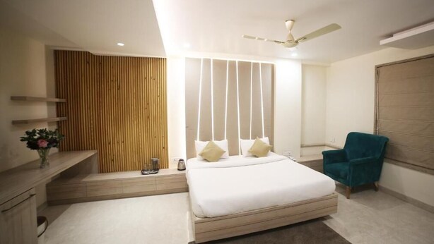 A modern bedroom with a large bed, a ceiling fan, a bedside table, a chair, and a wooden panel wall.