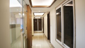 A hallway with a glass wall on the left, wooden paneling on the ceiling, and large windows on the right.