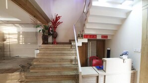 A reception area with a staircase leading to an upper floor, a reception desk, and a red chair.