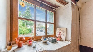 Interior rústico com janela para a vegetação, uma estante com cerâmica e uma pintura.