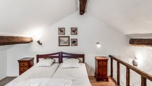 Quarto com teto de madeira, uma cama de casal com roupa de cama branca, duas mesas de cabeceira, um penteou de madeira e obras de arte na parede.