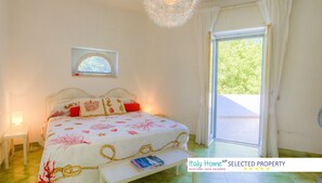 A bedroom with a bed, a bedside table, a window, and a view of greenery outside.