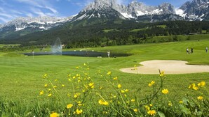 A golf course with a lake, mountains, and a clear sky.