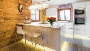 A modern kitchen with a wooden accent wall, a central island with bar stools, a chandelier, and built-in appliances.