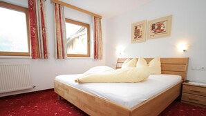A neatly made bed with a wooden headboard, a red carpeted floor, a window with curtains, and two wall-mounted light fixtures. - Spacious Apartment in Uderns near Ski Area (Uderns)