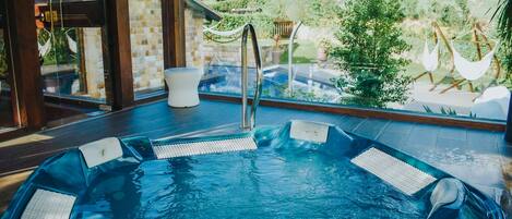 A hot tub with a view of a garden and a pool outside.