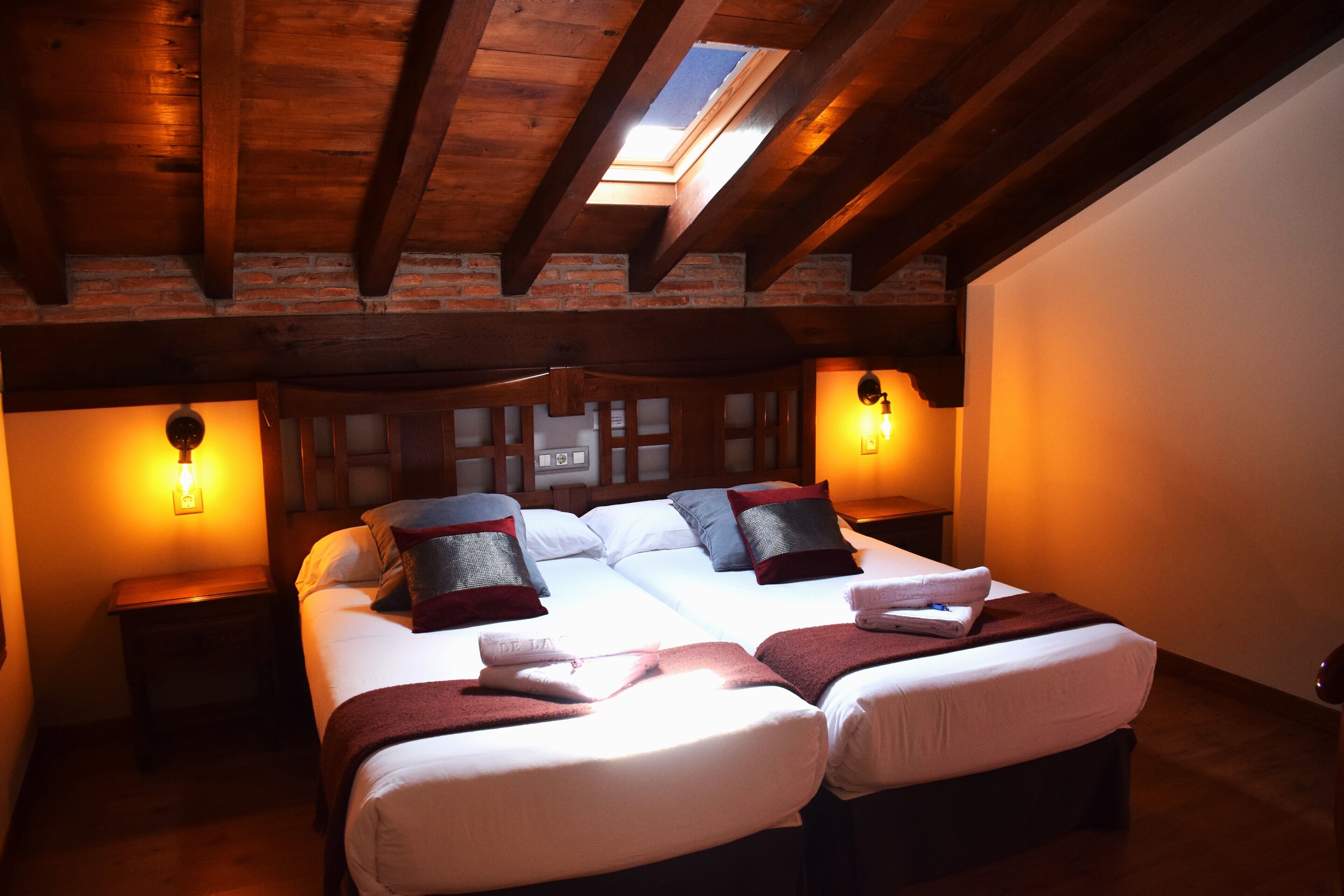 A cozy bedroom with a large bed, two bedside tables, and a skylight above.