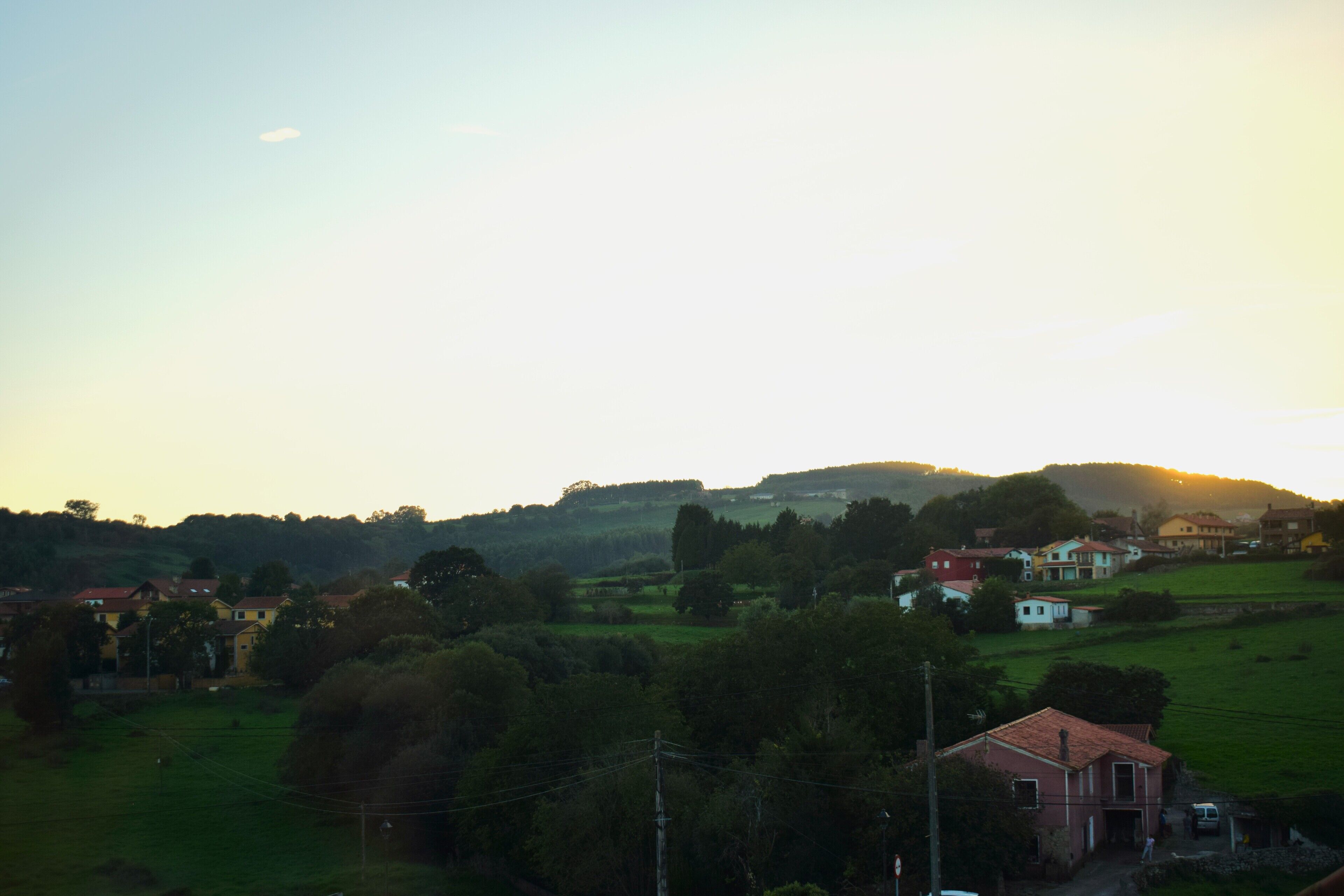Un paysage rural avec des maisons et de la végétation, où l’on distingue, au premier plan, un bâtiment imposant doté d’un toit rouge.
