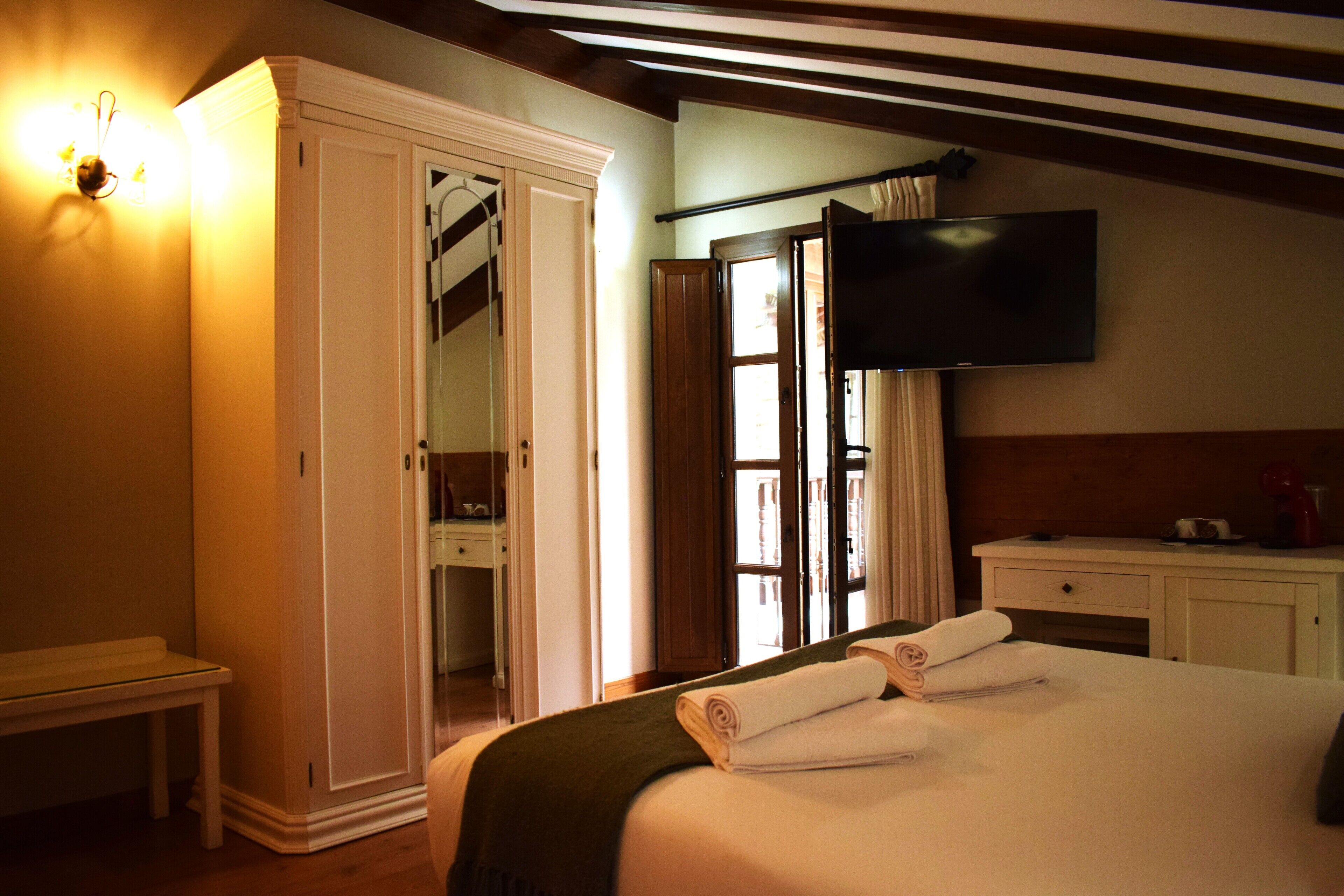 A hotel room with a bed, a TV, a wardrobe, and a desk.
