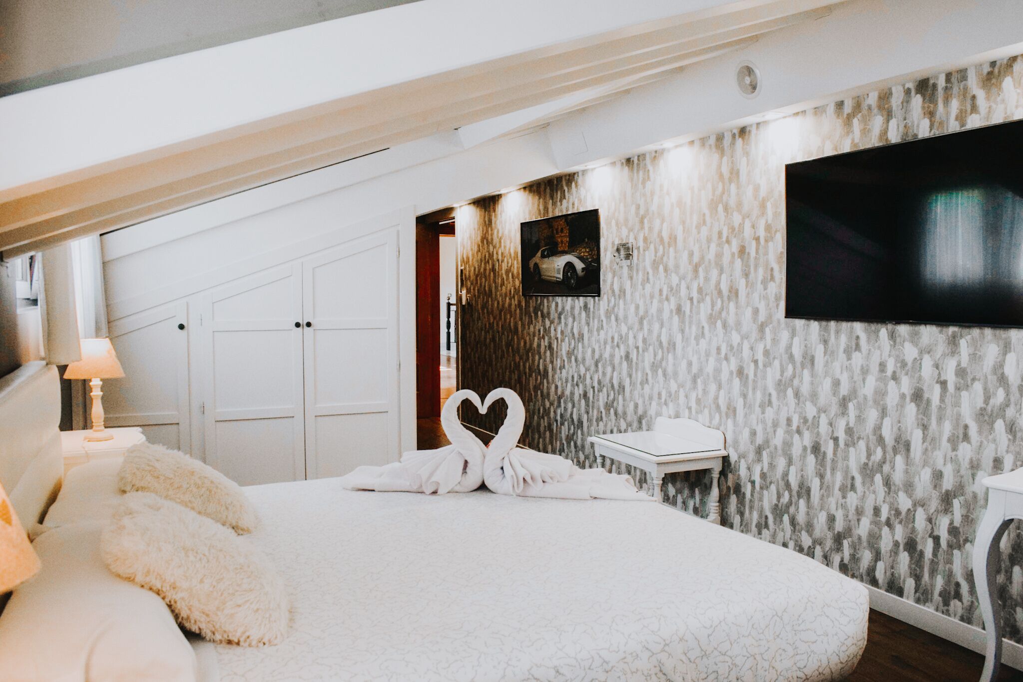 Ein Schlafzimmer mit einem großen Bett, einem an der Wand montierten Fernseher und einer Holztreppe zu einem Kleiderschrank.