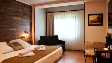 A hotel room with a bed, a sofa, a dining table, and a chair.