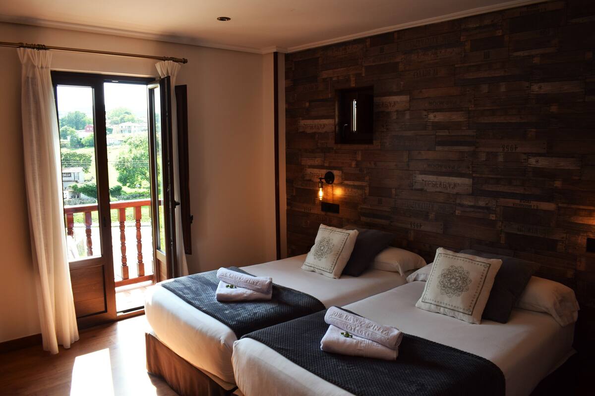 Une chambre d’hôtel avec deux lits, un balcon, un mur en bois et une vue sur la ville.