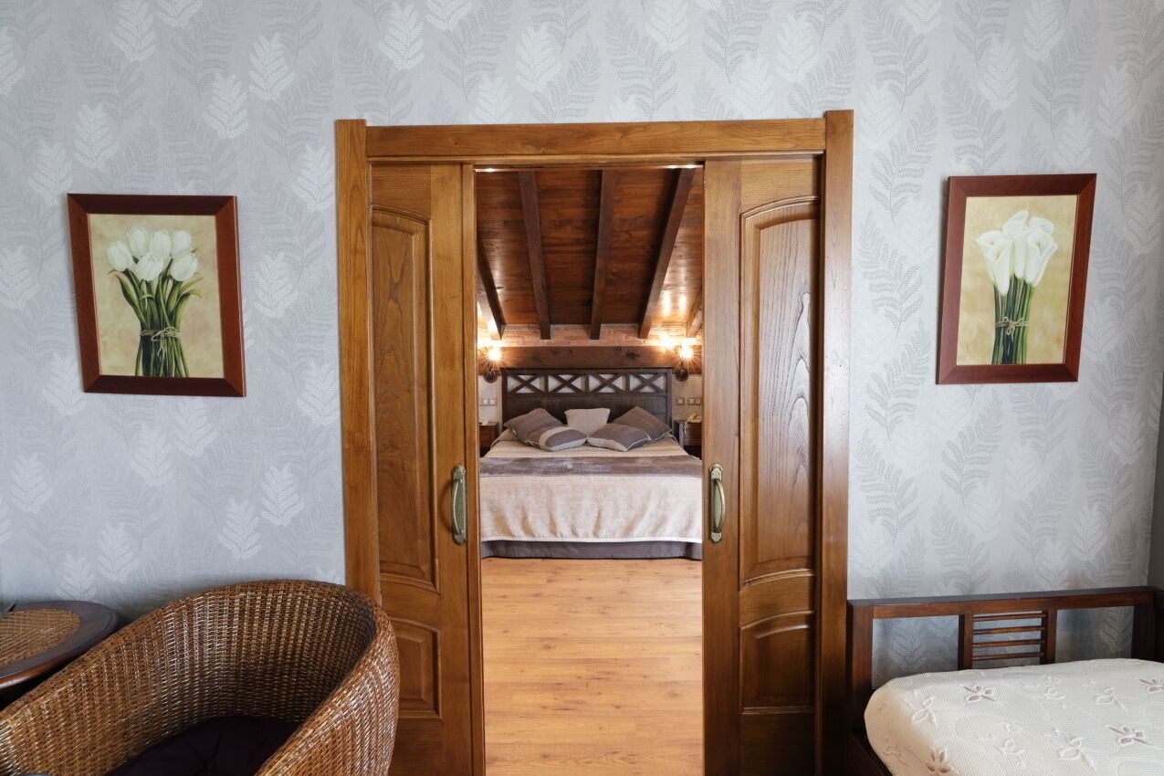 A room with a bed, a wicker chair, and a wooden door leading to another room.