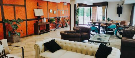 A modern living room with a beige sofa, brown armchairs, and a coffee table. There is a dining area with a table and chairs, and a bicycle in the background.
