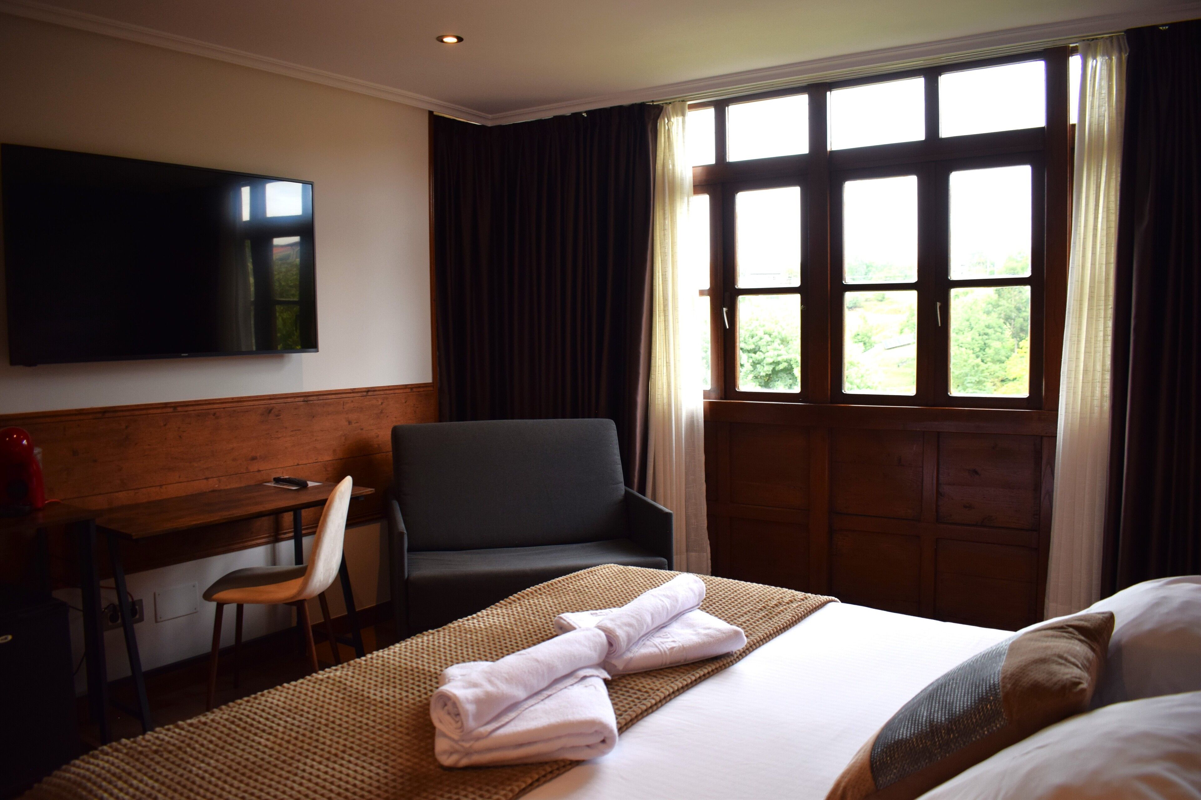 Hotelkamer met een bed, een bureau met stoel, een televisie en een raam met gordijnen.