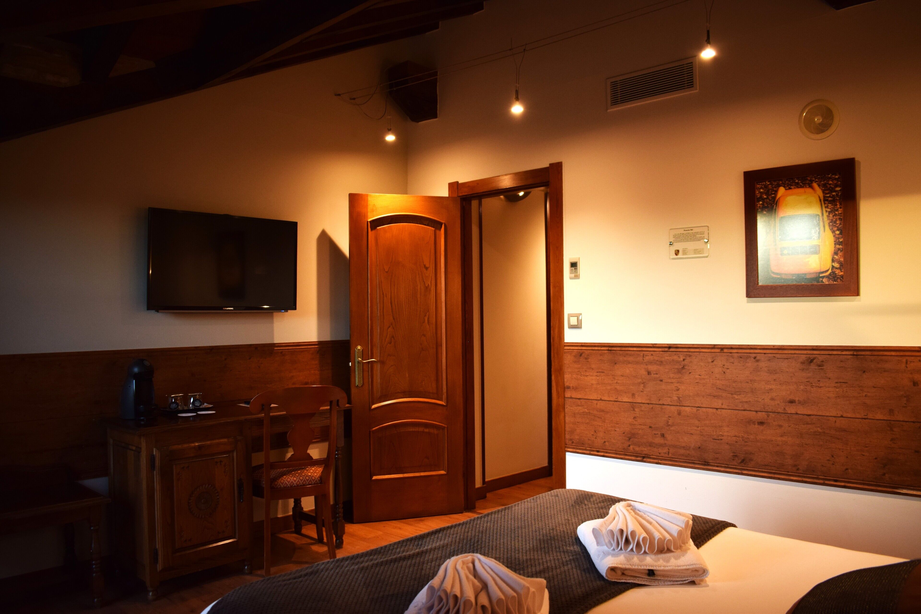 A hotel room with a bed, a desk with a chair, a television on the wall, and a door.