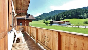A wooden balcony with a view of a rural landscape, including a house and mountains. - Unique Chalet in the Center of Elmau Near the Ski Lift (Ellmau)