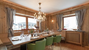 A wooden-paneled dining room with a large table set for six, green chairs, a chandelier, and a view of the outdoors through large windows. - Unique Chalet in the Center of Elmau Near the Ski Lift (Ellmau)